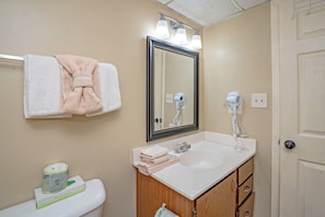 A bathroom with a toilet, sink, mirror, towel rack, and a hairdryer mounted on the wall. - Oak Square 205 is a spacious 2BR condo in downtown Gatlinburg (Gatlinburg)