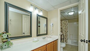 Un baño con lavamanos blanco, armarios de madera, un espejo grande y una zona de ducha.