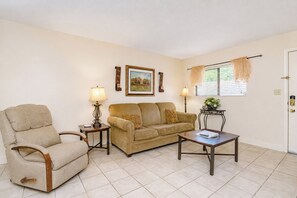 A living room with a beige armchair, a sofa, a coffee table, two side tables with lamps, a framed picture on the wall, and a window with curtains. - Oak Square 205 is a spacious 2BR condo in downtown Gatlinburg (Gatlinburg)