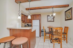 A kitchen with wooden cabinets, a refrigerator, a microwave, and a dining area with a table and chairs. - Oak Square 205 is a spacious 2BR condo in downtown Gatlinburg (Gatlinburg)