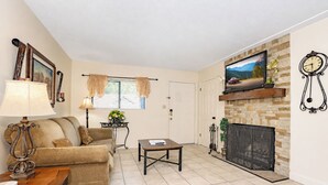 Una sala de estar con sofá, mesa de centro, chimenea, televisor y reloj.