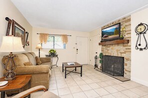 Una sala de estar con sofá, mesa de centro, chimenea, televisor y reloj.