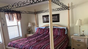 A four-poster bed with a red and white patterned bedspread, a nightstand with a lamp, and a framed quote on the wall.