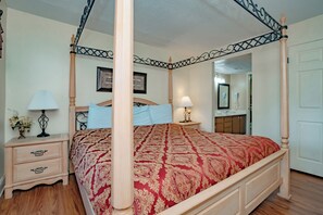 A four-poster bed with a patterned bedspread, bedside tables with lamps, a dresser, and a mirror.