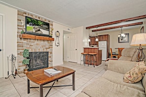 A living room with a fireplace, a television mounted on the wall, a kitchen area with wooden cabinets, and a dining area with a table and chairs. - Oak Square 205 is a spacious 2BR condo in downtown Gatlinburg (Gatlinburg)