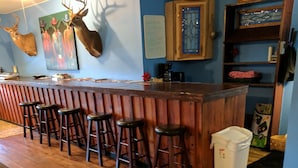 Un espace bar avec des tabourets en bois, un comptoir et des têtes de cerf fixées au mur.
