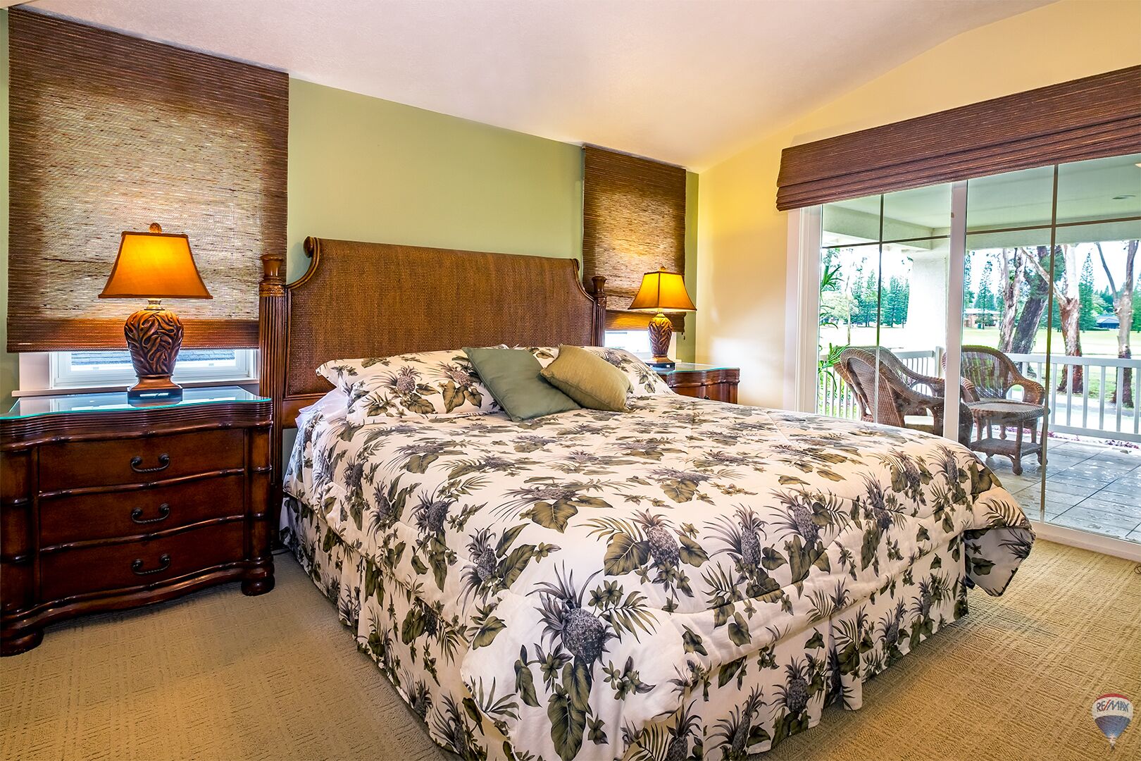 A hotel room with a large bed, two nightstands with lamps, a wooden headboard, and a view of a balcony with outdoor furniture.