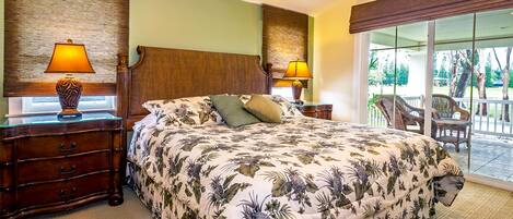 A hotel room with a large bed, two nightstands with lamps, a wooden headboard, and a view of a balcony with outdoor furniture.