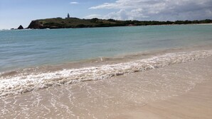 Una spiaggia con acque cristalline, una riva sabbiosa e un faro in lontananza.