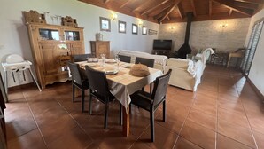 Un comedor con una mesa de madera dispuesta para cuatro personas, rodeada de sillas de mimbre. Se observa un sofá blanco y un televisor al fondo.