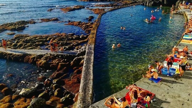 Zona costera con aguas cristalinas, formaciones rocosas y un muelle.