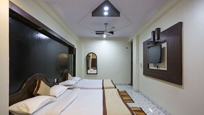 Habitación de hotel con dos camas, ventilador de techo, televisor montado en la pared y un espejo.