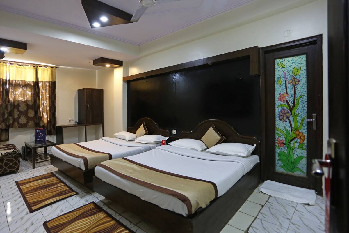 A hotel room with two beds, a wardrobe, a desk, and a bathroom door with a floral design.