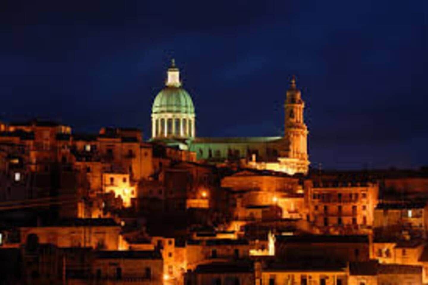 A cityscape at night with illuminated buildings and a prominent dome and tower structure.