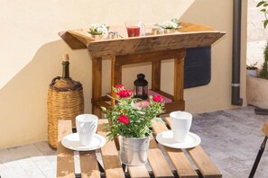 Une table en bois, avec des tasses blanches et un seau en métal contenant des fleurs rouges.