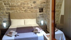 A bedroom with a stone wall, a bed with a beige headboard, two bedside tables with lamps, and a wooden wardrobe. - Old Market House Antò Ragusa (Ragusa)