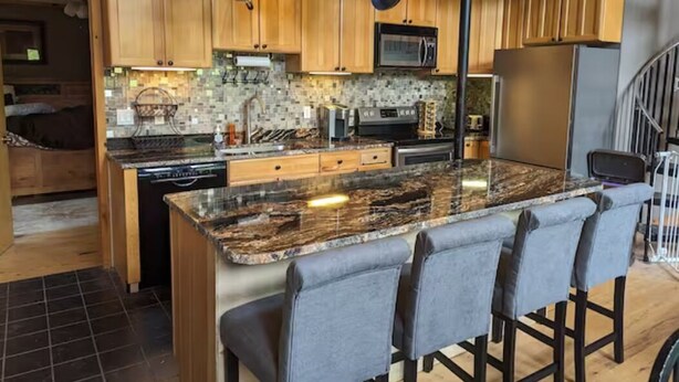 Una cocina moderna con armarios de madera, una isla de granito con taburetes altos y utensilios colgando.