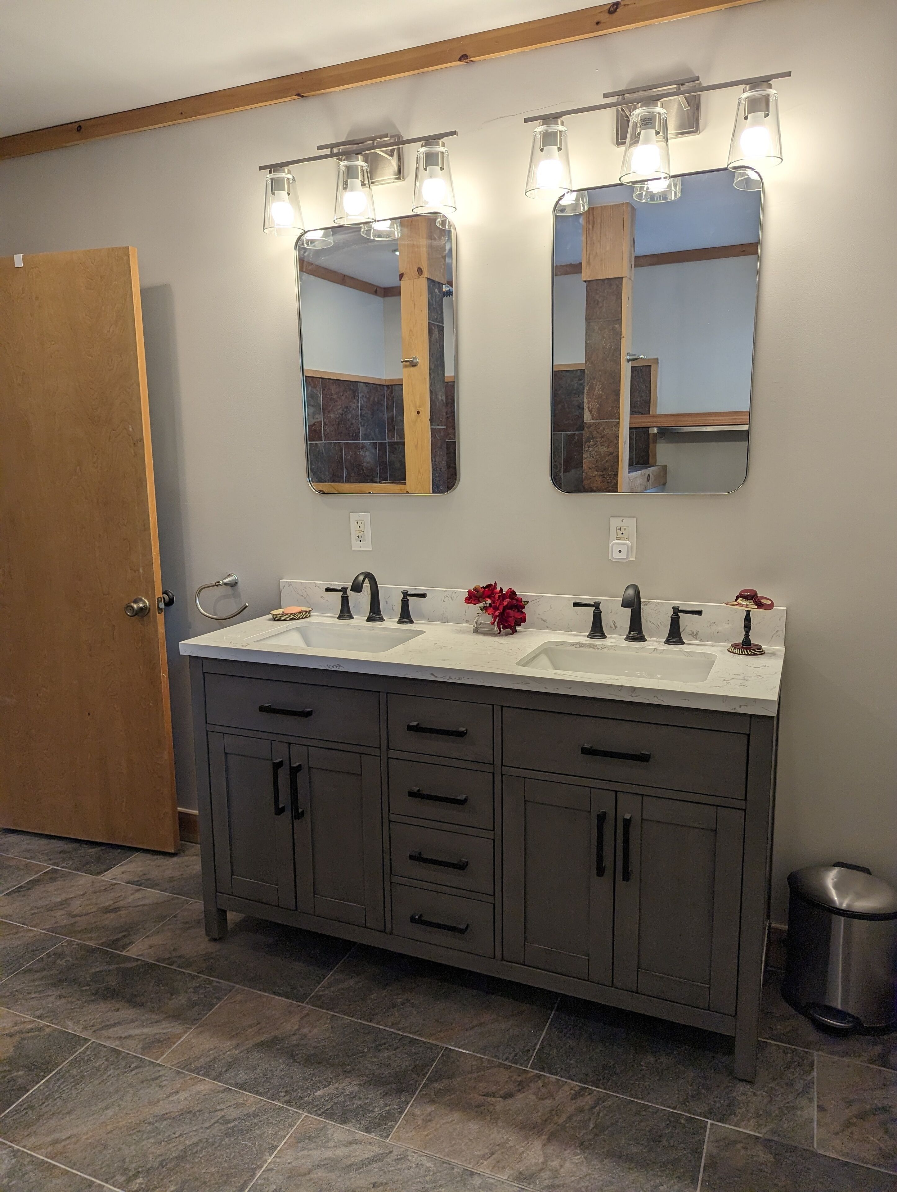A bathroom with a double sink vanity, two wall-mounted mirrors, and a trash can.
