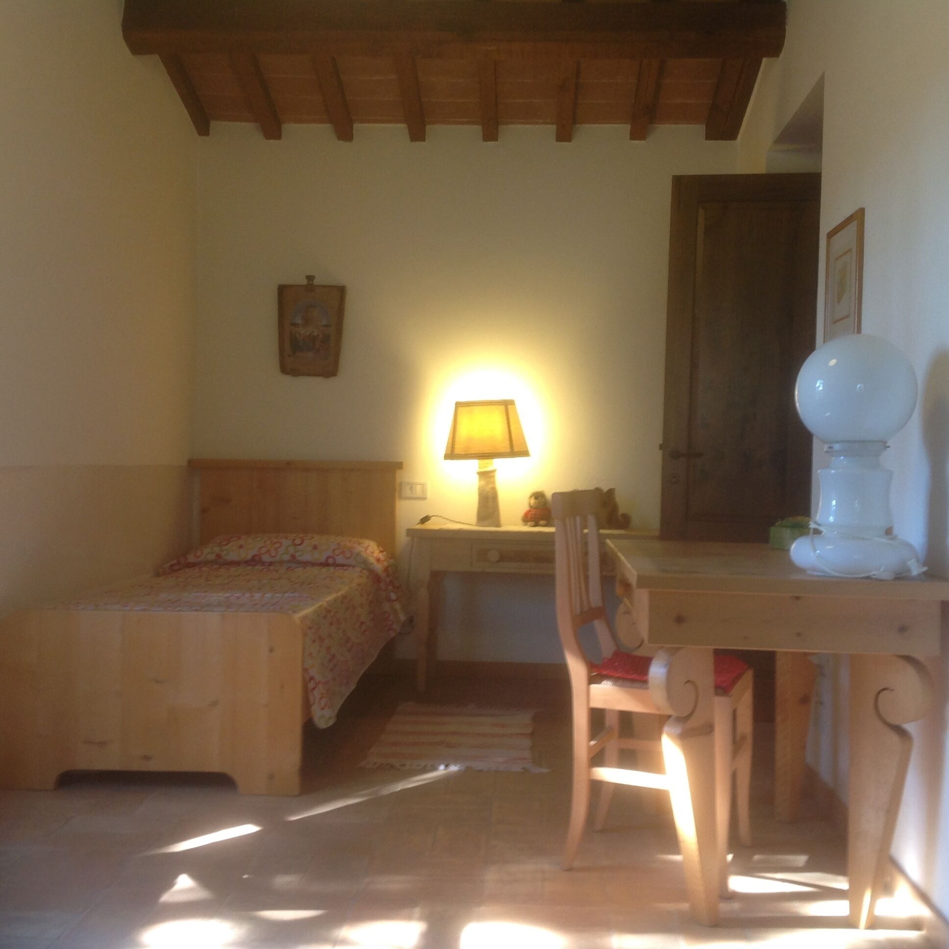 Um quarto com uma cama, uma escrivaninha, uma cadeira, um abajur e uma porta.