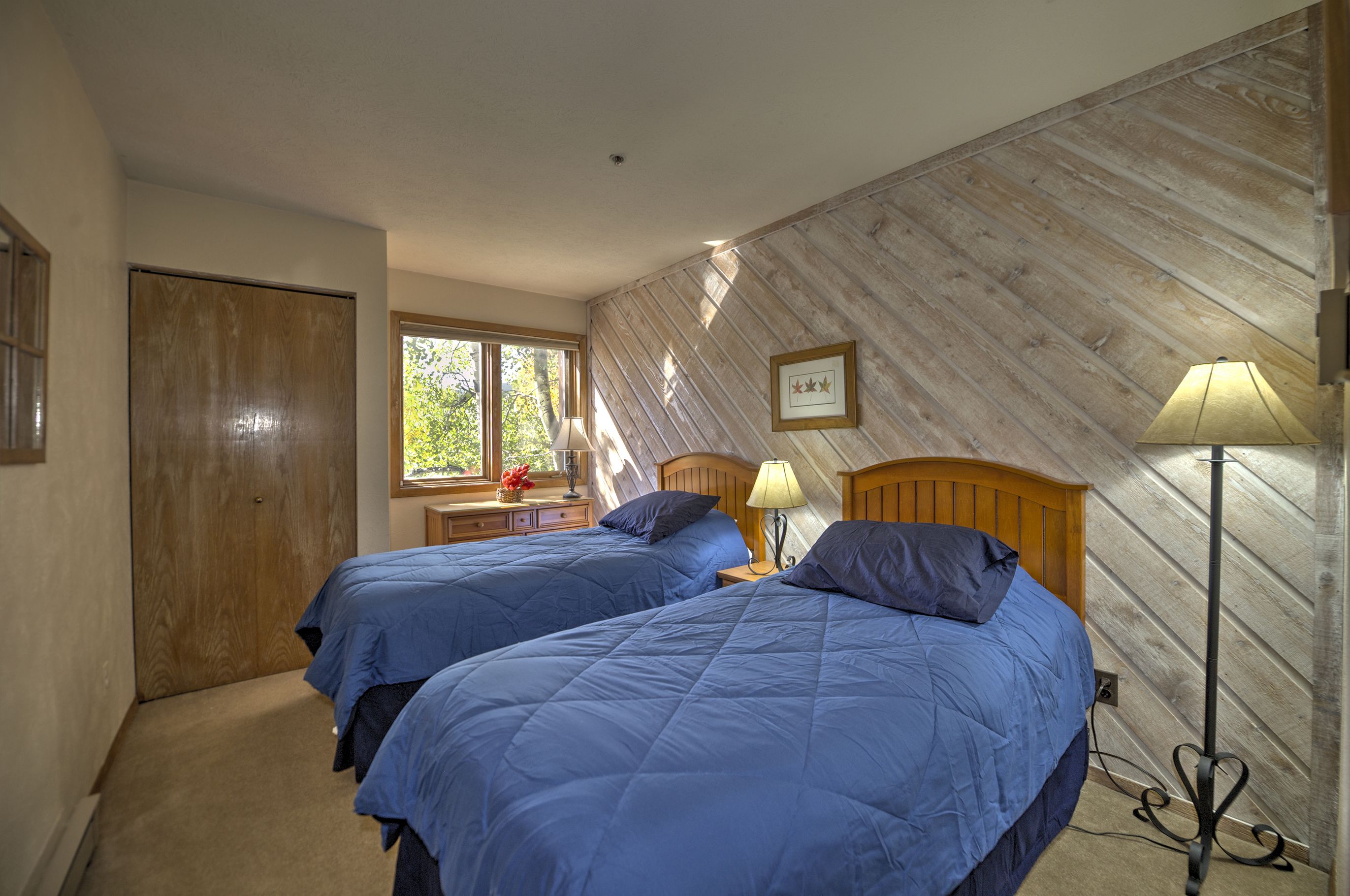 A bedroom with two beds, wooden headboards, a window with a view, and a lamp.