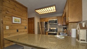 Una cocina con armarios de madera, un refrigerador de acero inoxidable, un microondas y una encimera de granito.