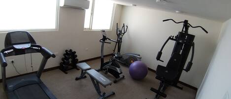 A gym with a treadmill, elliptical, bench press, dumbbells, and a medicine ball.