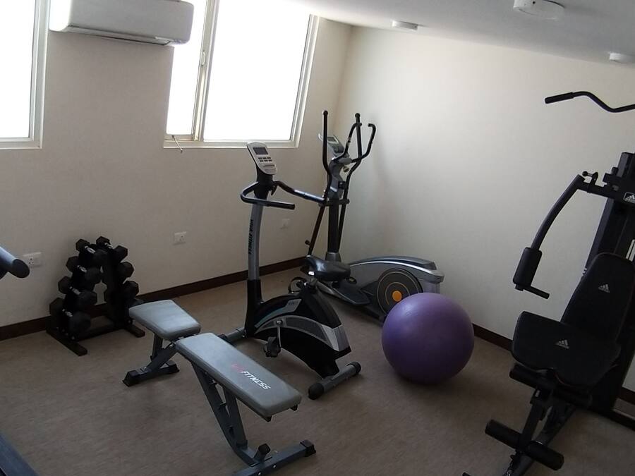 Un gimnasio con cinta de correr, elíptica, banco de pesas, mancuernas y balón medicinal.