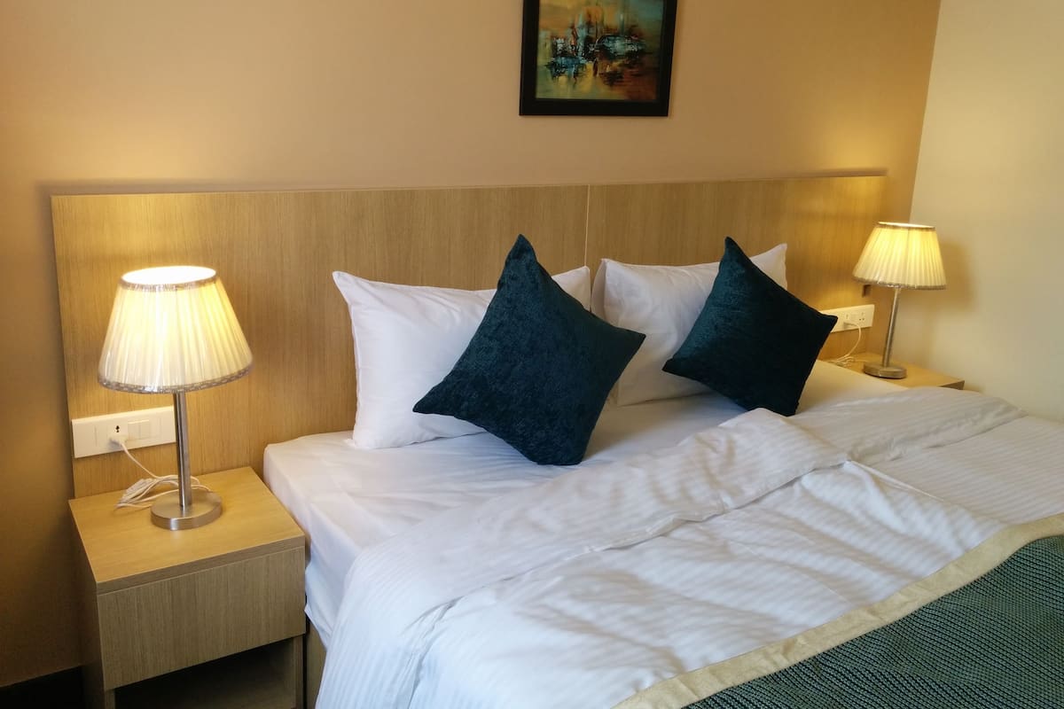 A hotel room with a neatly made bed, two bedside lamps, and a painting on the wall.
