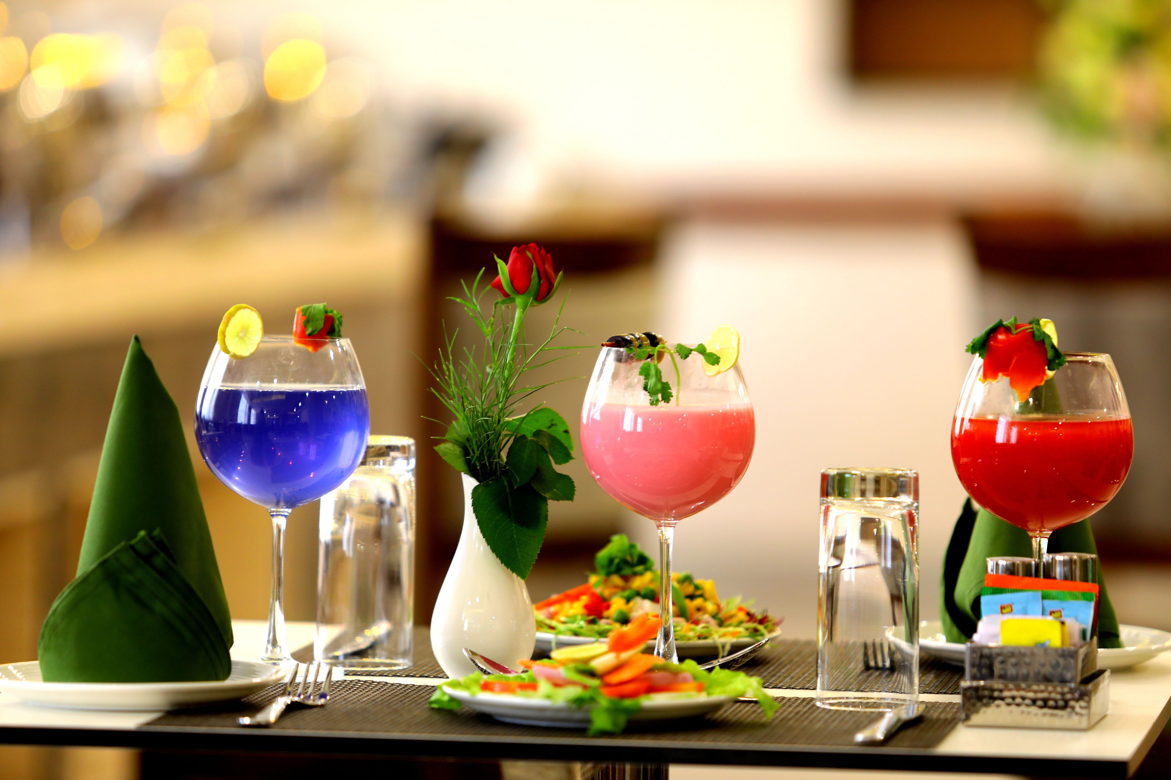 Une table dressée avec diverses boissons, une salade et un vase rempli de verdure.