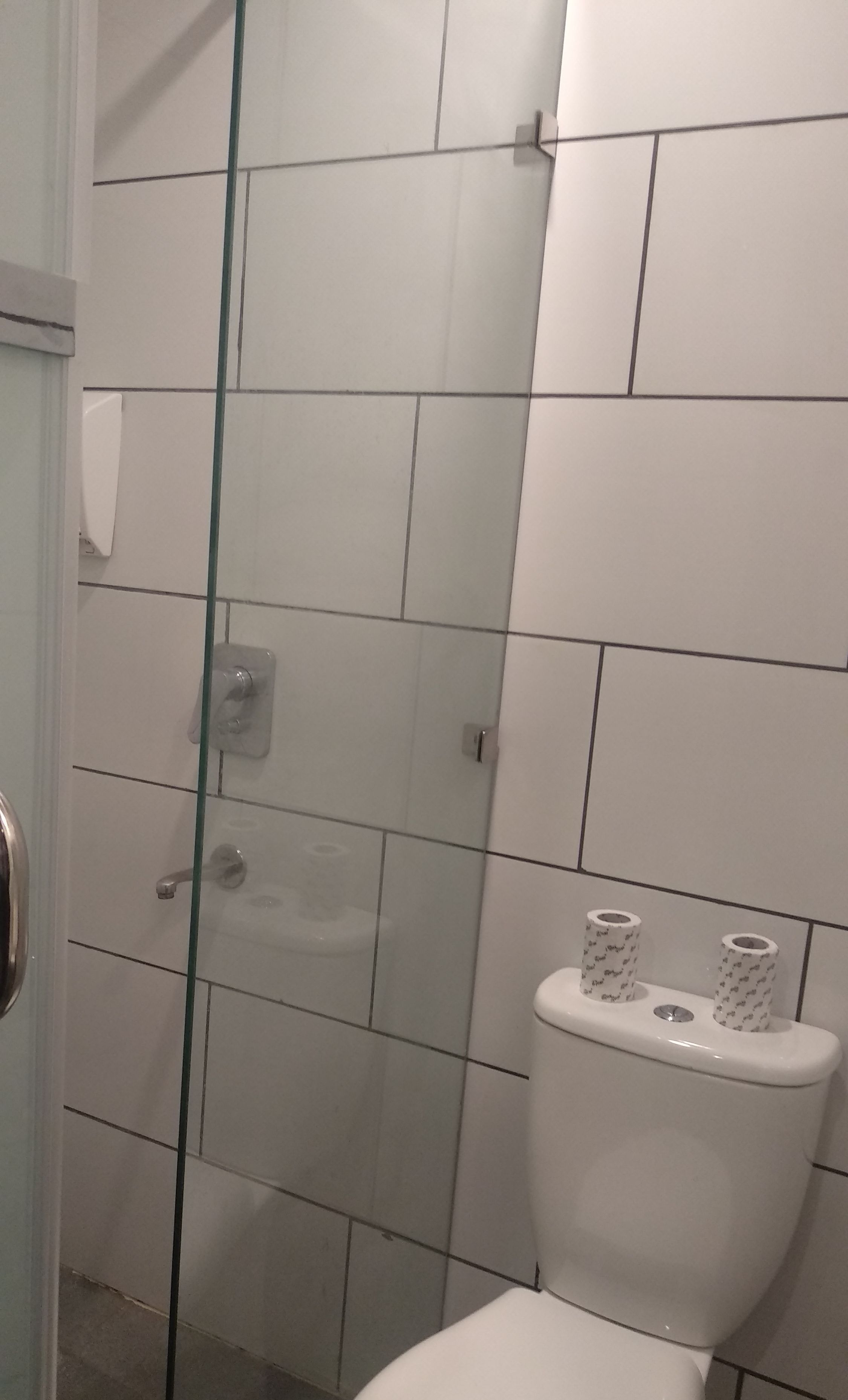 A bathroom with white tiles, a glass shower enclosure, and a toilet with toilet paper.