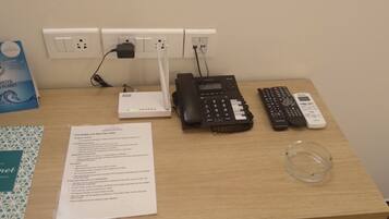 A desk with a Starlet Suites Gourmet restaurant menu, a fire safety and security letter, a Netia router, a Samsung and a Philips phone, and a glass container.