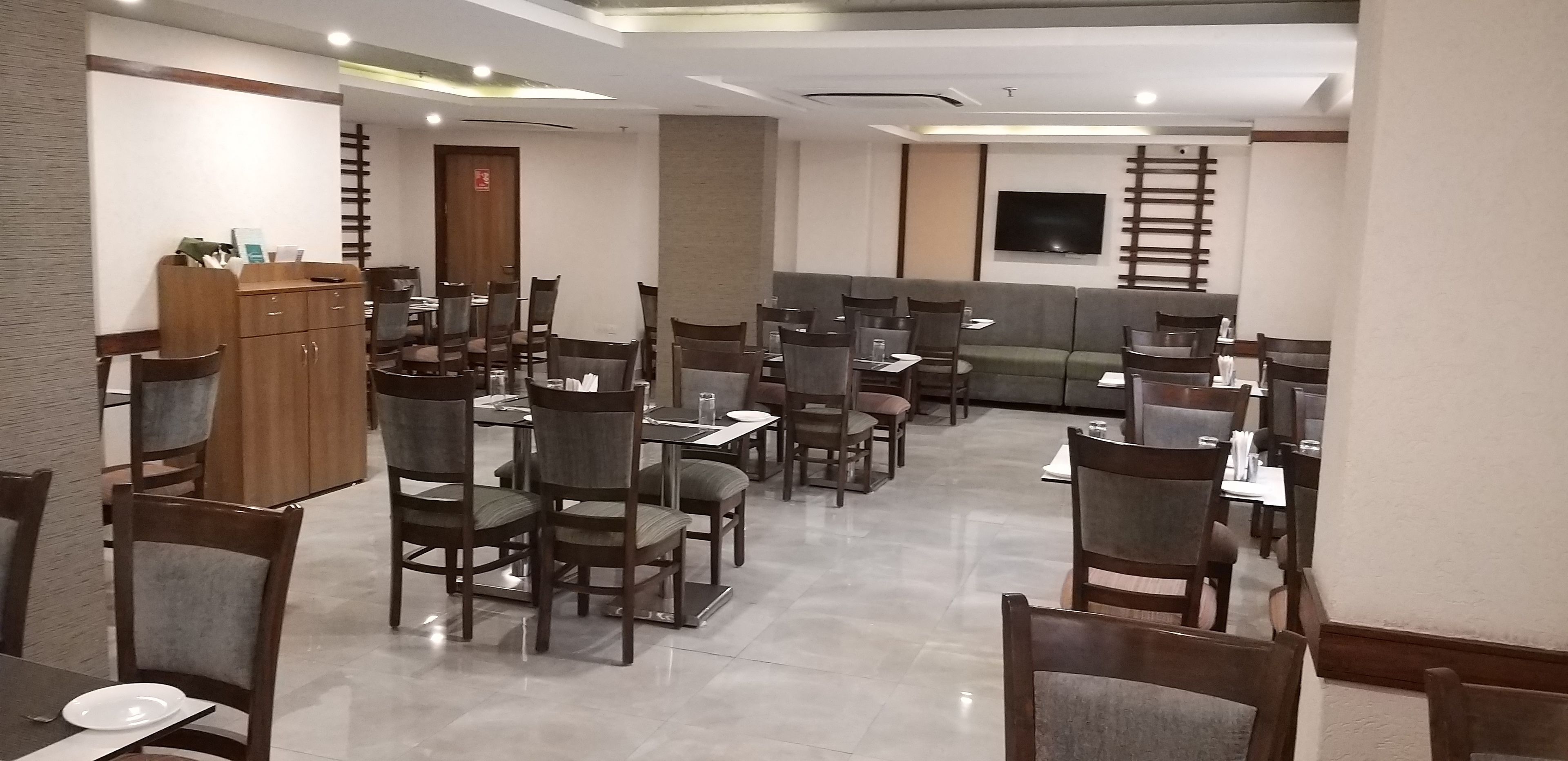 Un área de comedor con varias mesas y sillas, un sofá y un televisor instalado en la pared.