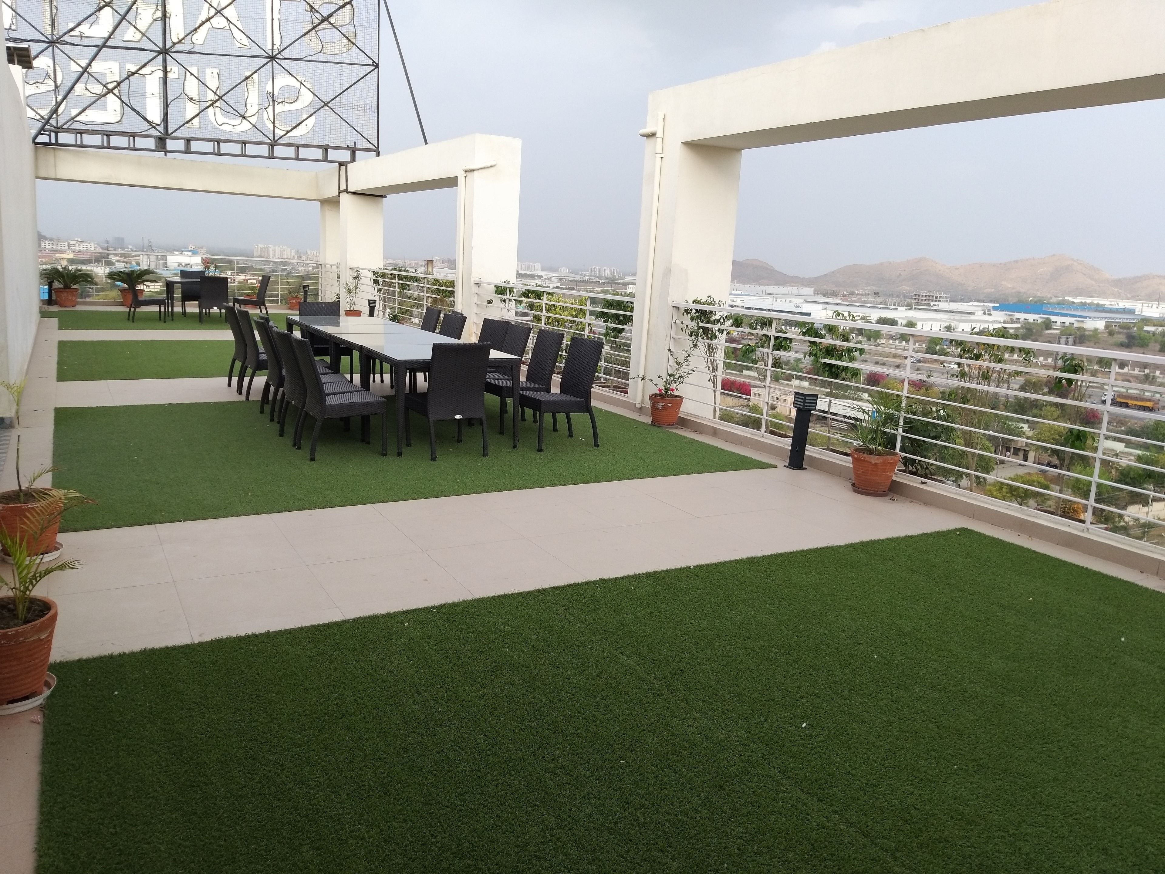 Una terraza en la azotea con comedor, césped artificial, plantas en macetas y vistas de la ciudad.