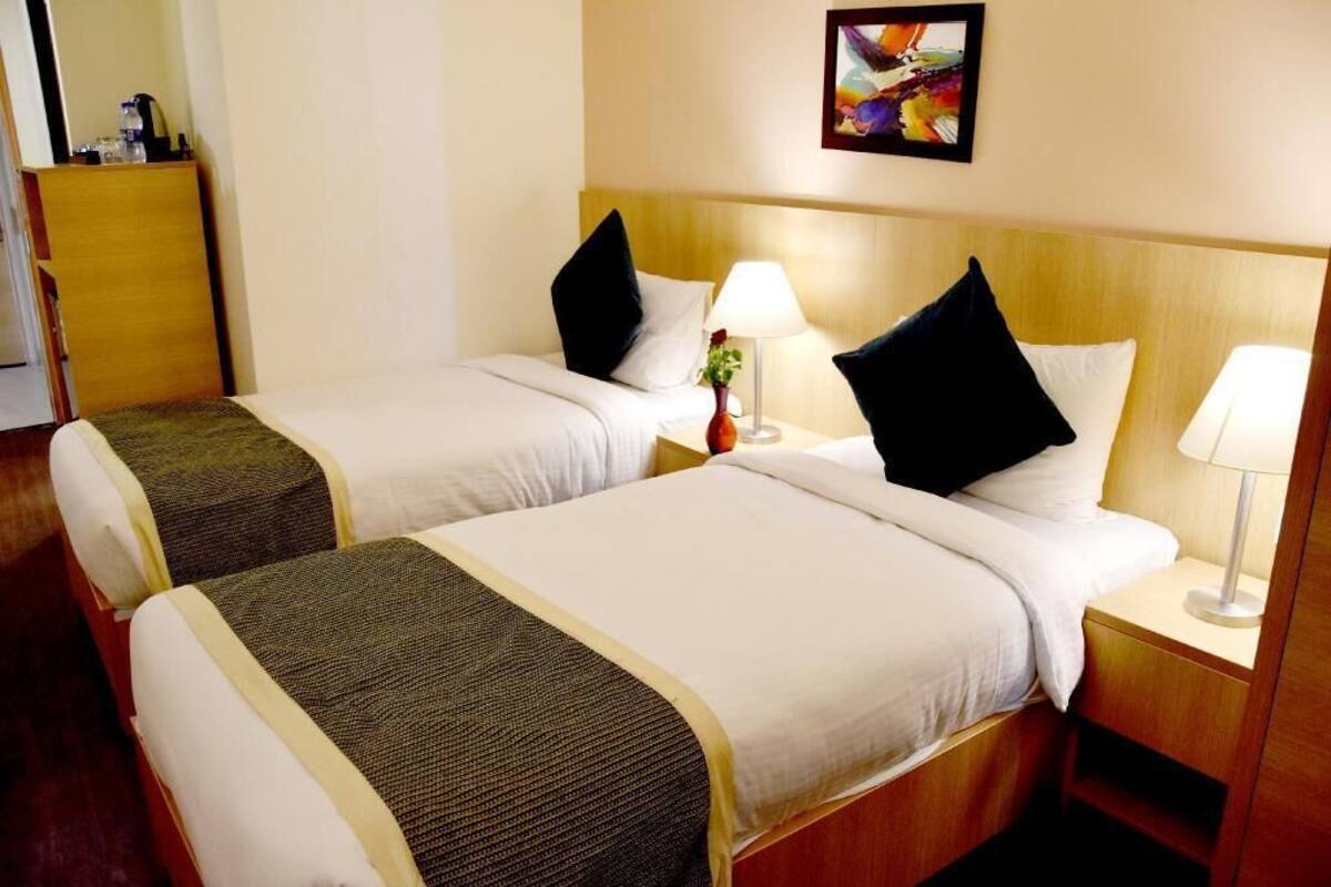 A hotel room with two beds, each with a pillow, a bedside table with a lamp, and a painting on the wall.
