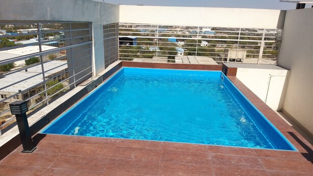 A rectangular swimming pool with a tiled deck, surrounded by a metal railing. - Starlit Suites Neemrana (Neemrana)