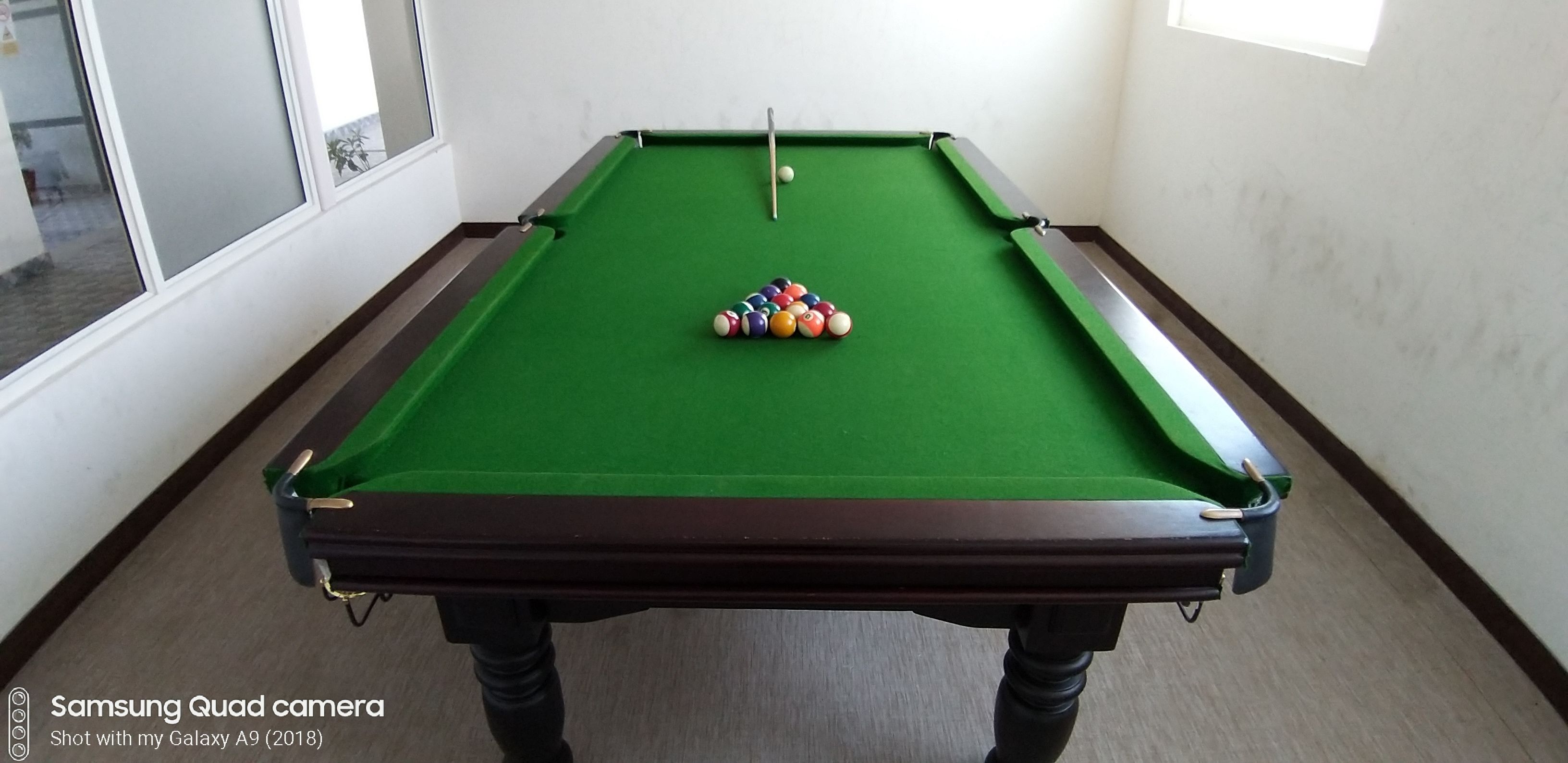 A pool table with balls and cues, a window, and a door.