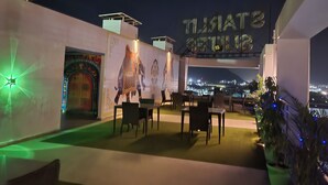 An outdoor seating area with a mural of an elephant, a sign reading "THAI SEA VIEW," and a view of the cityscape in the background. - Starlit Suites Neemrana (Neemrana)