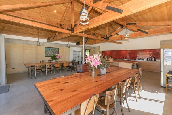 A spacious dining area with a long wooden table and chairs, a kitchen area with red brick backsplash, and a hanging light fixture. - Oasis Yurt Lodge (Wanaka)