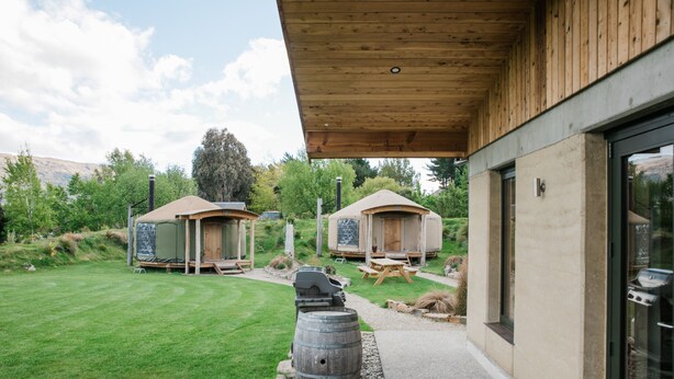 Un espacio exterior moderno con construcciones de madera, una parrilla y un barril.