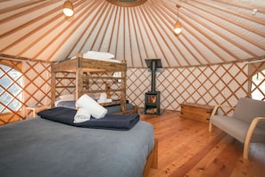 A yurt interior with a bunk bed, a sofa, a fireplace, and wooden lattice walls. - Oasis Yurt Lodge (Wanaka)