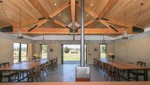 Una habitación amplia con una larga mesa de madera y sillas, ventanas grandes y un equipo de aire acondicionado central.