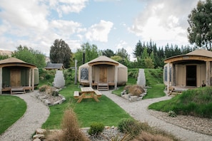 Three wooden cabins with a picnic table in the center, surrounded by a gravel path and greenery. - Oasis Yurt Lodge (Wanaka)