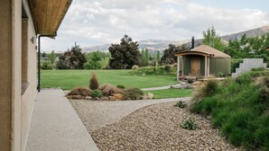 Una casa moderna con un espacio exterior cubierto, un césped cuidado y vistas a montañas distantes.