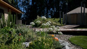 Un jardín con diversas plantas y flores, una terraza de madera y un edificio al fondo.