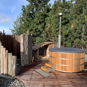 A wooden deck leading to a sauna with a metal chimney, surrounded by a wooden fence and pine trees. - Oasis Yurt Lodge (Wanaka)