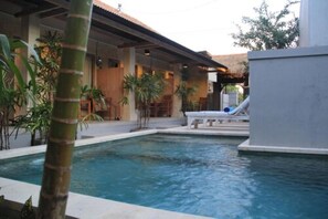 A pool area with a lounge chair and palm trees. - Sadana Bali Guest House (Denpasar)