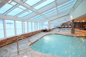 An indoor swimming pool with a glass ceiling, stone flooring, and a view of the outside.