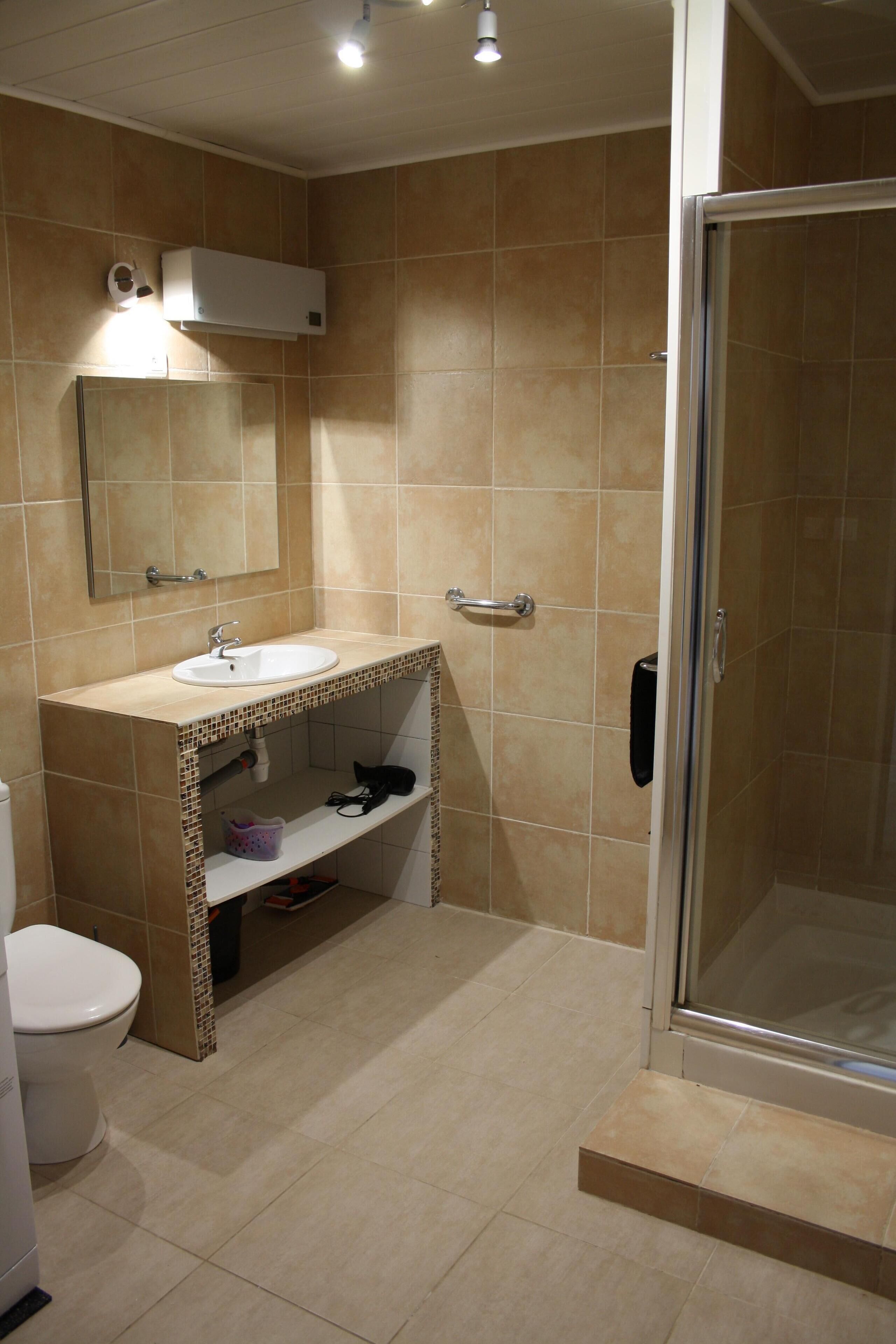Un baño con un lavamanos blanco, un espejo, un inodoro y una zona de ducha.