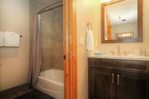 A bathroom with a bathtub, a shower, a vanity with a mirror, and a towel rack. - Southern Comfort (Breckenridge)
