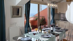 A dining area with a table set for four, a view of the outdoors, and a kitchen in the background. - Spacious 4 BR apartment, Taormina center, multiple terraces w. stunning views  (Taormina)